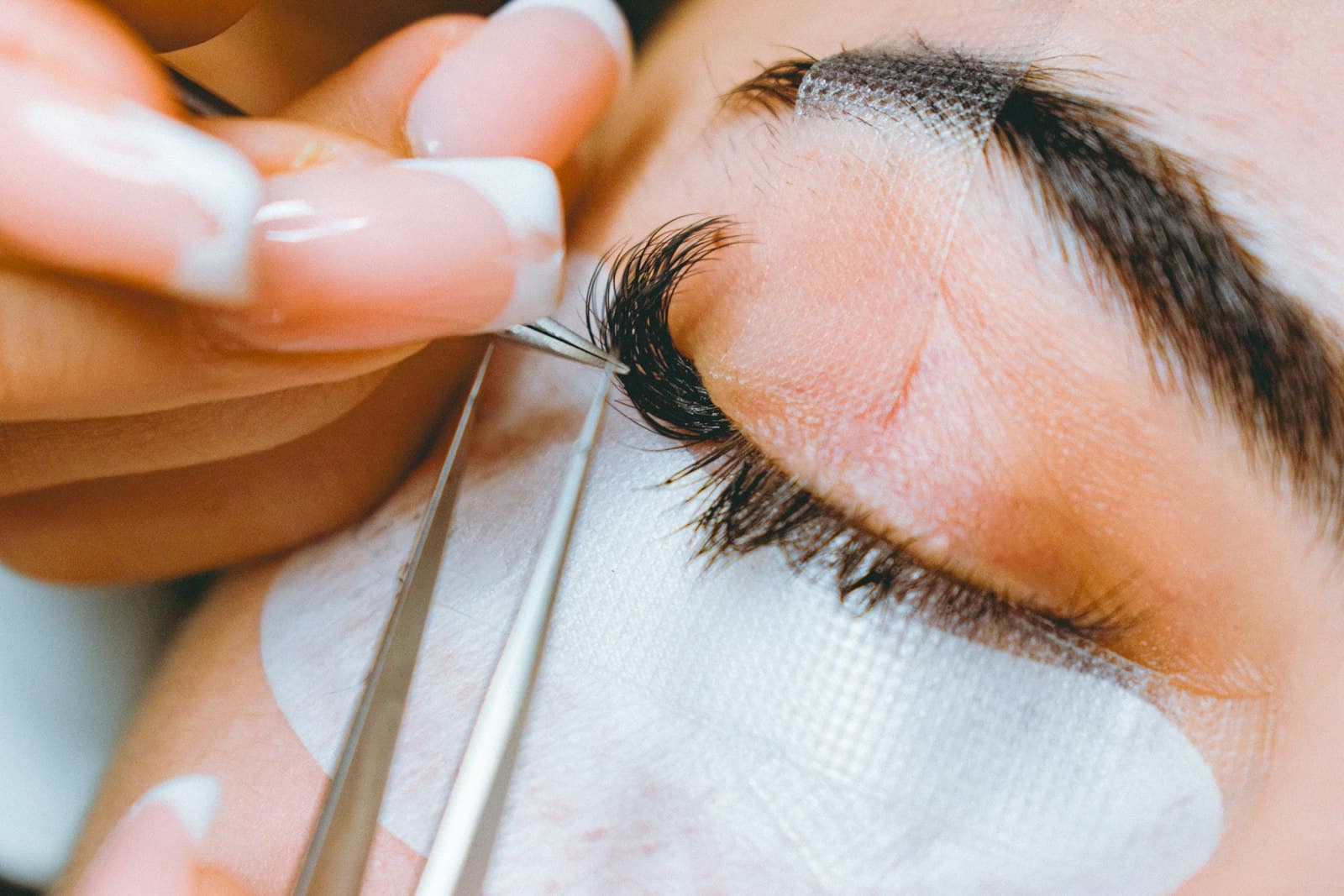A lash technician applying an individual extension with tweezers